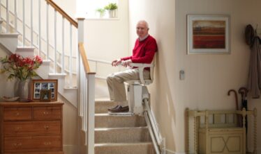Ηλικιωμένος άνδρας χαρούμενος καθώς κατεβαίνει τις σκάλες με τον ανελκυστήρα σκαλών Stannah